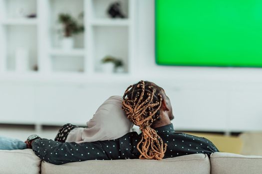 African Couple Sitting On Sofa Watching TV Together Chroma Green Screen Woman Wearing Islamic Hijab Clothes. High quality photo