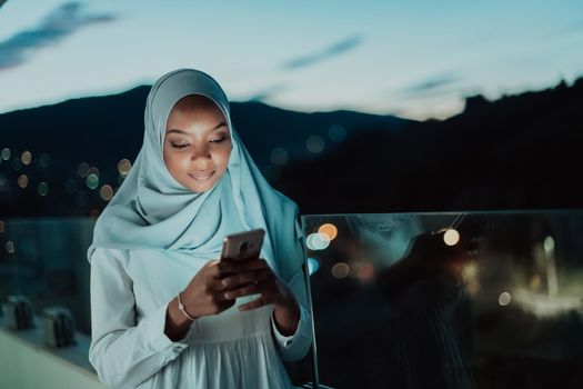 Young Muslim woman wearing scarf veil on urban city street at night texting on a smartphone with bokeh city light in the background. High-quality photo