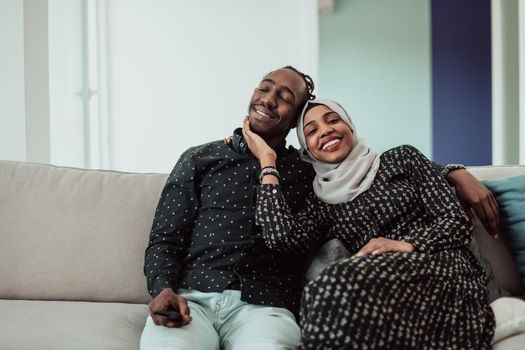 African Couple Sitting On Sofa Watching TV Together. Women Wearing Islamic Hijab Clothes. High-quality photo