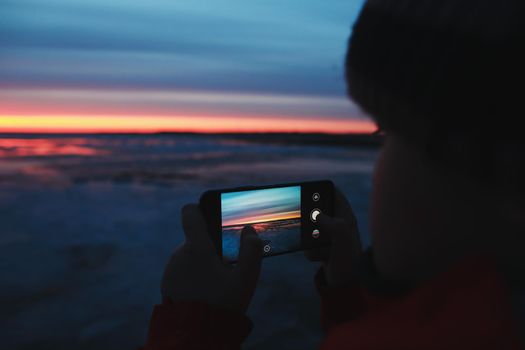 Man hands with mobile cell phone taking a photo of sunset sky at sea. Gradient color. Sky texture. Beautiful abstract nature sunset as background.