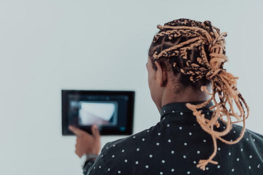 Smiling African American man using modern smart home system, controller on wall, positive young man switching temperature on thermostat or activating security alarm in apartment. High quality photo