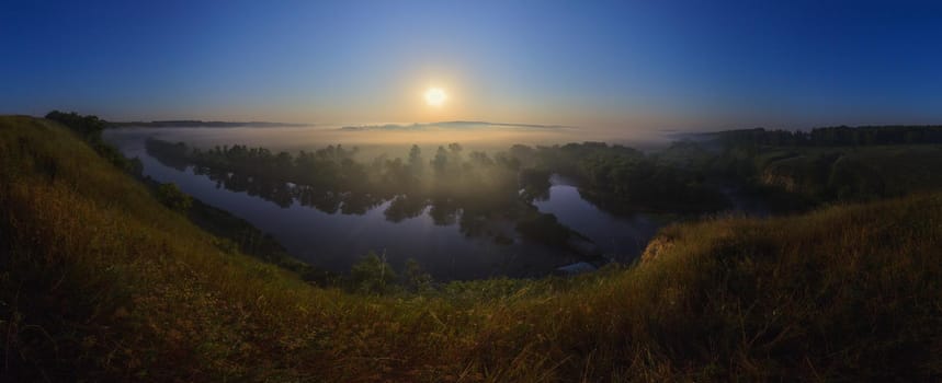Foggy morning sunrise on river at summer wide angle landscape panorama.