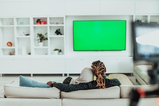 African Couple Sitting On Sofa Watching TV Together Chroma Green Screen Woman Wearing Islamic Hijab Clothes. High quality photo