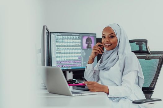 Young Afro-American modern Muslim businesswoman wearing a scarf in a creative bright office workplace with a big screen. High-quality photo