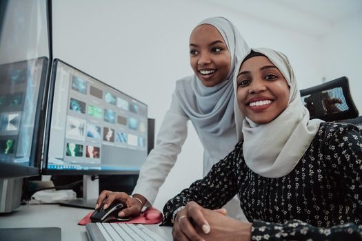 Friends at the office are two young Afro-American modern Muslim businesswomen wearing scarfs in a creative bright office workplace with a big screen. High-quality photo