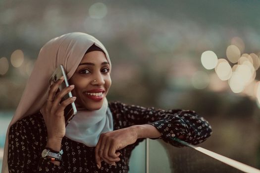 Young Muslim woman wearing scarf veil on urban city street at night texting on a smartphone with bokeh city light in the background. High-quality photo