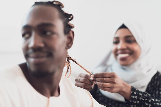 A young Muslim couple has a romantic time at home while the woman makes the hairstyle for her husband female wearing traditional Sudan Islamic hijab clothes. High-quality photo