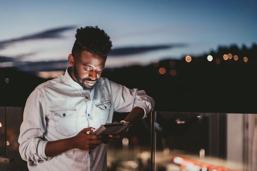 The young man on an urban city street at night texting on a smartphone with bokeh and neon city lights in the background. High-quality photo. High-quality photo