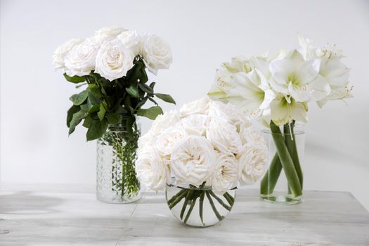 White roses, lily, in round vases with two cups of coffee on the table for a special occasion as a kitchen decoration. Copy space