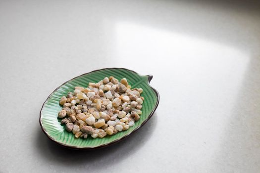 Plate in the form of a green leaf with small stones. Copy space