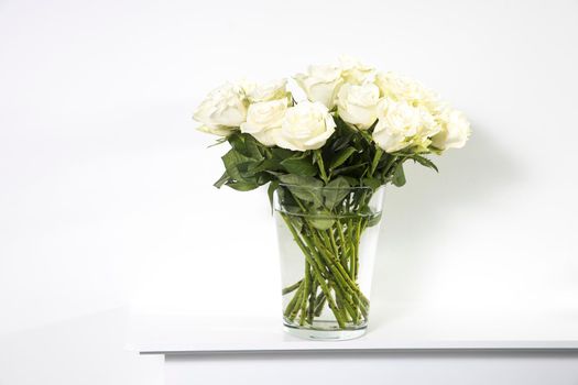 A bouquet of white roses in a vintage glass vase on a white panel of a fake fireplace.