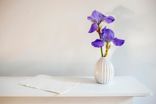 Blue iris in a corrugated vase with a piece of craft paper on a white table. Place for text