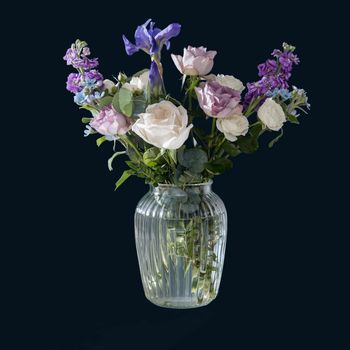 Bouquet of hackelia velutina, purple and white roses, small tea roses, matthiola incana and blue iris in glass vase isolated on black background