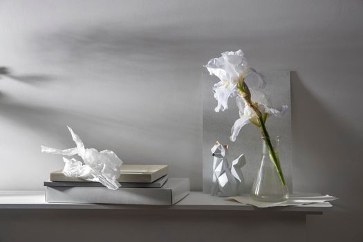 White iris flower in a transparent vase on a background of gray watercolor paper, a fox figurine, notepads and boxes on the table. Place for your text.