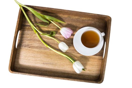 A bouquet of multicolored tulips and a cup of tea are on a wooden tray on the table. Copy space