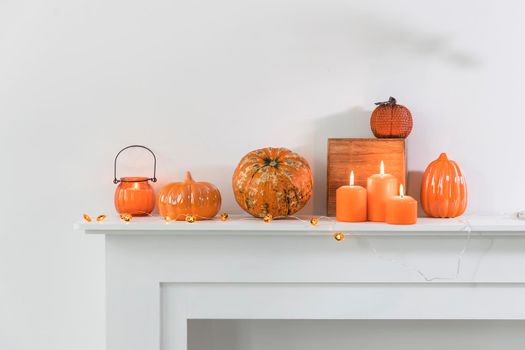 Porcelain and natural pumpkins, orange candles on a white table, Halloween decorations.