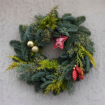 Christmas wreath of fir branches with decorations, star, balls hanging on the grey wall of the house
