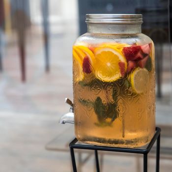 Orange, strawberry, lemon and mint lemonade in a large jar with a tap on the table at a banquet