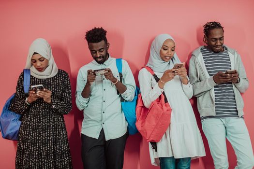 A group of African Muslim students using smartphones while standing in front of a pink background. High-quality photo