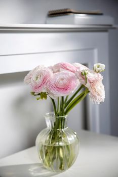 the bouquet of pale pink Persian buttercups in the glass vase on the table against the background of the fireplace.