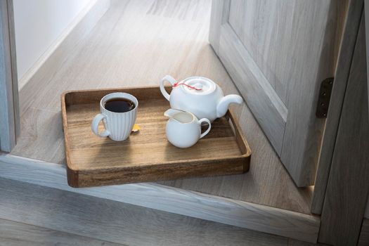 A wooden tray with a cup of tea, a teapot, a milk jug is on the floor in the doorway.