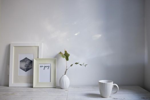 Scandinavian style. Interior Design. A white cup, a small vase with a dried eucalyptus branch, a two photo frames are on the table. Copy space for text