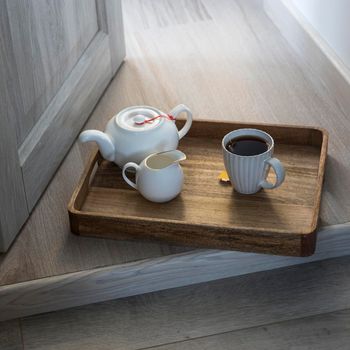 A wooden tray with a cup of tea, a teapot, a milk jug is on the floor in the doorway.