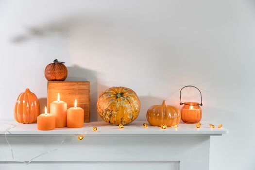 Porcelain and natural pumpkins, orange candles on a white table, Halloween decorations.