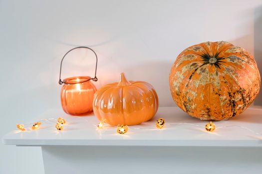 Porcelain and natural pumpkins, orange candles on a white table, Halloween decorations.