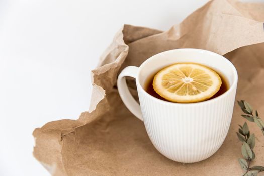 White corrugated cup with tea and lemon are on brown craft paper on a wooden table.