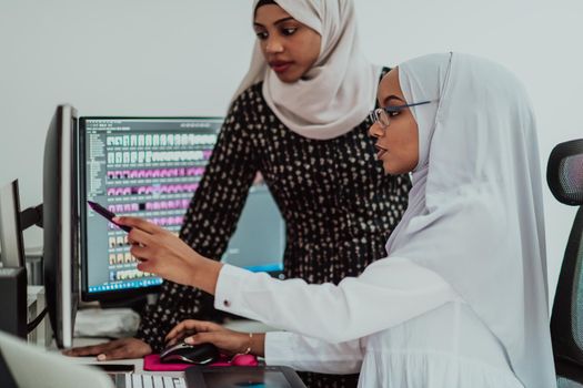 Friends at the office are two young Afro-American modern Muslim businesswomen wearing scarfs in a creative bright office workplace with a big screen. High-quality photo