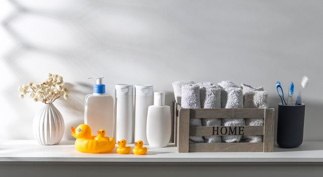 Shelf in the bathroom. Bouquet of gypsophila in white corrugated vase in style of the seventies, bottles of shampoo and cream, small face towels in container and yellow rubber ducks are on the shelf.