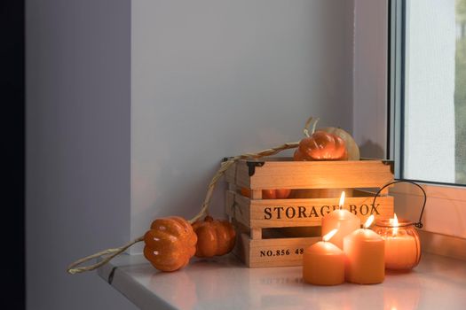 Preparing your home for Halloween. A wooden pumpkin box, a faux pumpkin garland, orange candles, a cup of tea and a candle lantern decorate the window.