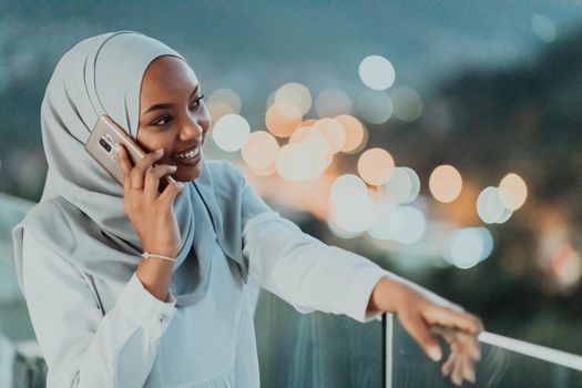 Young Muslim woman wearing scarf veil on urban city street at night texting on a smartphone with bokeh city light in the background. High-quality photo