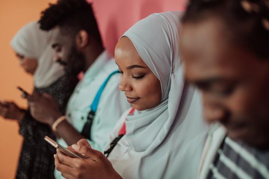 A group of African Muslim students using smartphones while standing in front of a yellow background. High-quality photo