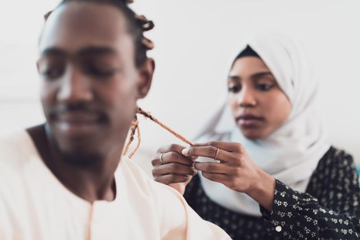 A young Muslim couple has a romantic time at home while the woman makes the hairstyle for her husband female wearing traditional Sudan Islamic hijab clothes. High-quality photo