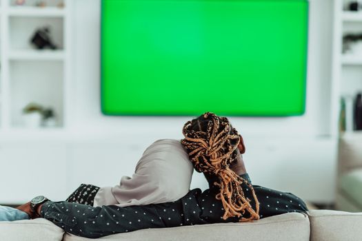 African Couple Sitting On Sofa Watching TV Together Chroma Green Screen Woman Wearing Islamic Hijab Clothes. High quality photo