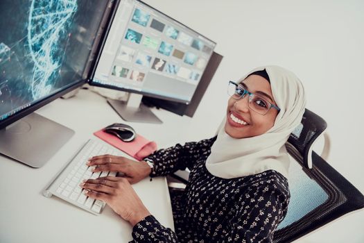 Young Afro-American modern Muslim businesswoman wearing a scarf in a creative bright office workplace with a big screen. High-quality photo