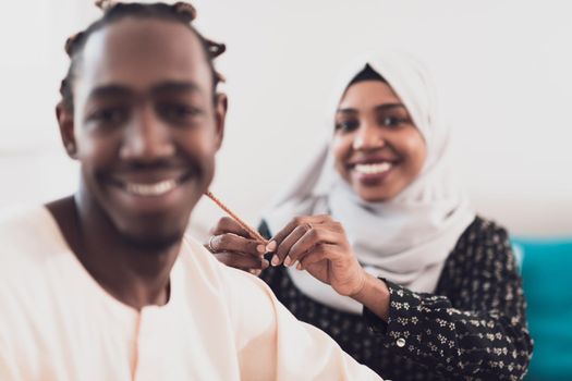 A young Muslim couple has a romantic time at home while the woman makes the hairstyle for her husband female wearing traditional Sudan Islamic hijab clothes. High-quality photo