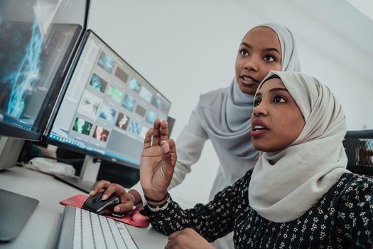 Friends at the office are two young Afro-American modern Muslim businesswomen wearing scarfs in a creative bright office workplace with a big screen. High-quality photo