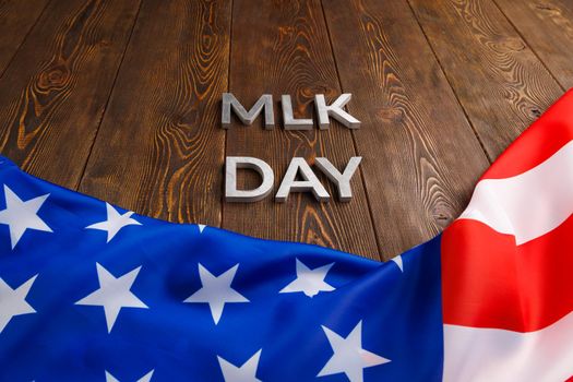 the word MLK day laid with silver metal letters on wooden surface with crumpled USA flag at lower side in linear perspective. MLK means Martin Luther King Jr.