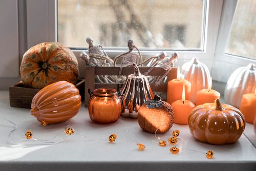 Porcelain and natural pumpkins, orange candles on a white table, Halloween decorations.