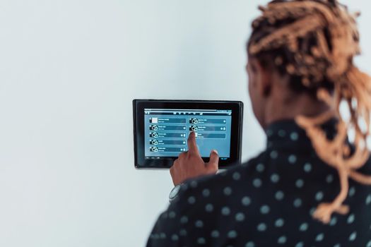 Smiling African American man using modern smart home system, controller on wall, positive young man switching temperature on thermostat or activating security alarm in apartment. High quality photo