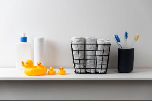 Shelf in the bathroom. Bouquet of gypsophila in white corrugated vase in style of the seventies, bottles of shampoo and cream, small face towels in container and yellow rubber ducks are on the shelf.