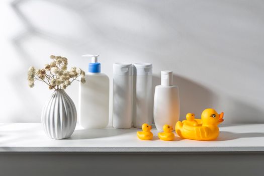 Shelf in the bathroom. Bouquet of gypsophila in white corrugated vase in style of the seventies, bottles of shampoo and cream, small face towels in container and yellow rubber ducks are on the shelf.