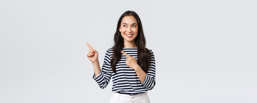 Lifestyle, people emotions concept. Excited good-looking asian girl smiling pleased as found excellent product, pointing fingers left at advertisement and looking satisfied, recommend promo.