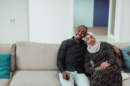 African Couple Sitting On Sofa Watching TV Together. Women Wearing Islamic Hijab Clothes. High-quality photo