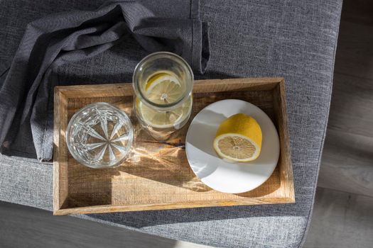 A refreshing glass of water, a bottle of water and a slice of lemon on a tray, a linen napkin, and half a lemon on a saucer to eat on the couch in the summer heat