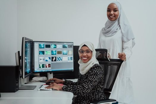 Friends at the office are two young Afro-American modern Muslim businesswomen wearing scarfs in a creative bright office workplace with a big screen. High-quality photo