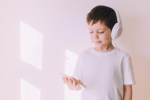 The boy listens to music with lifestyle headphones . Modern technologies. Kids and gadgets. Music for children. Modern children. Smartphones in children. Copy space. White background.